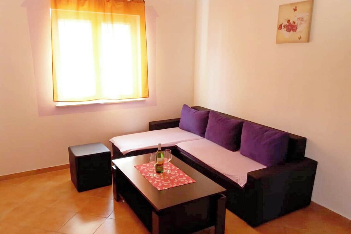 A small living area with a sofa, a coffee table, a small table, a window with curtains, and a wall-mounted picture.