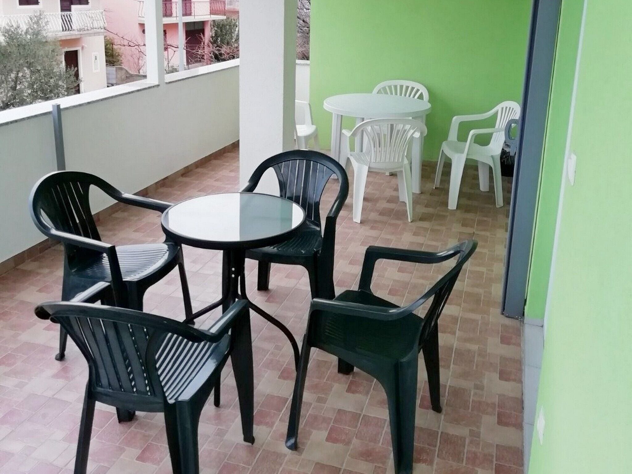 A balcony with a round table and four chairs, a small round table with two chairs, and a view of a pink building in the background.