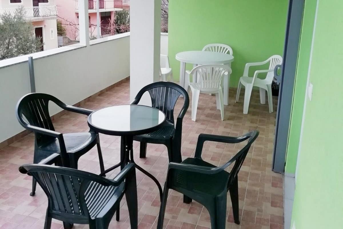 A balcony with a round table and four chairs, a small round table with two chairs, and a view of a pink building in the background.