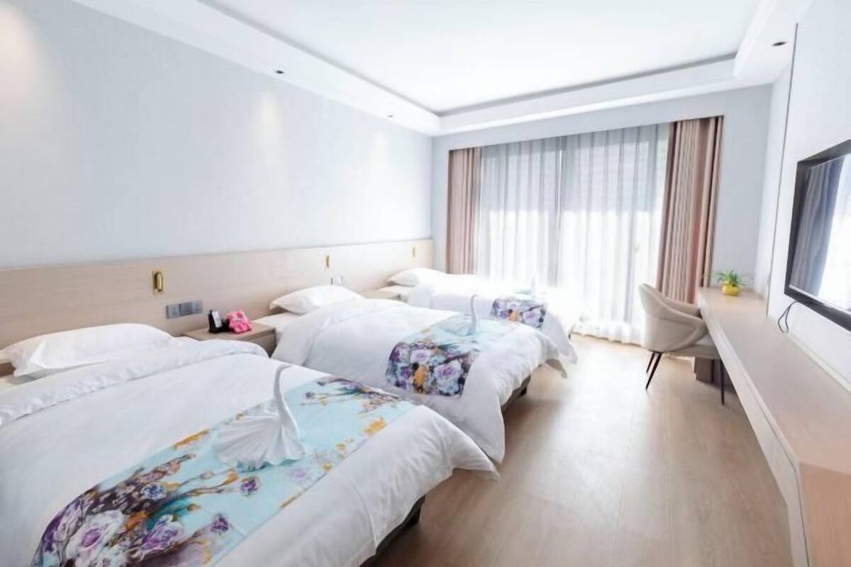 Een hotelkamer met twee bedden, een bureau en een groot raam met gordijnen.