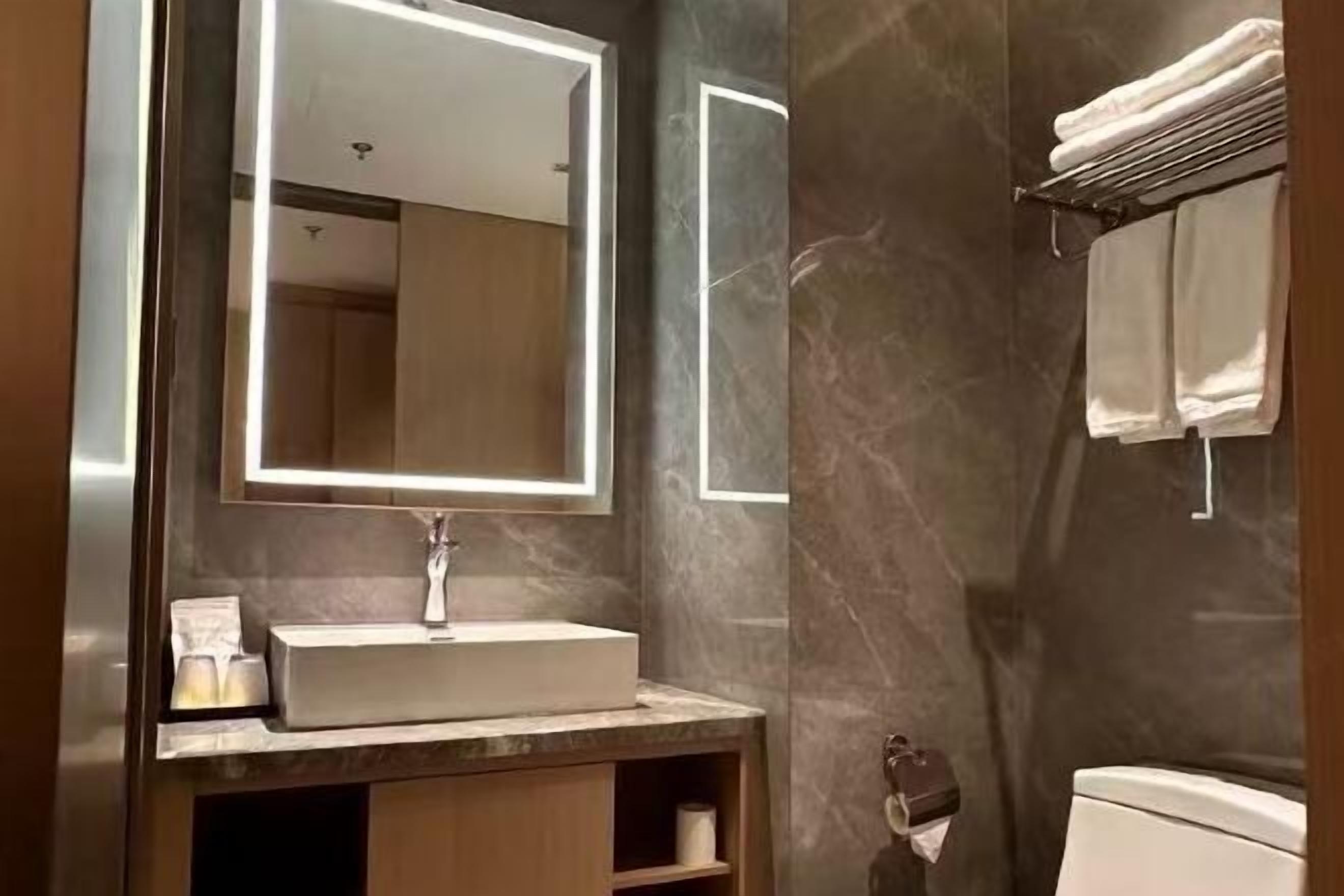 A bathroom with a marble wall, a sink with a mirror, and a towel rack.