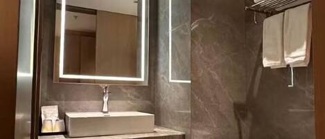 A bathroom with a marble wall, a sink with a mirror, and a towel rack.