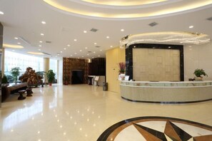 A spacious lobby with a reception desk, a large chandelier, and a decorative wall.