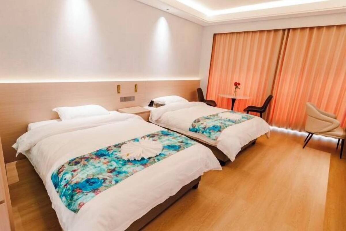 Een hotelkamer met twee bedden, een bureau, een stoel en een groot raam met gordijnen.