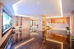 A modern hotel lobby with a polished marble floor, a reception desk, and a large TV screen. - Lvzhiyun International Hotel (Liuyang)
