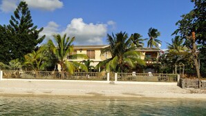 A beachfront property with a sandy beach, palm trees, and a house with a balcony.
