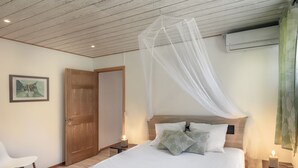 A bedroom with a bed, bedside tables, a nightstand, a chair, a door, and a wall-mounted air conditioner.