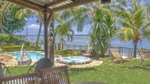 A covered outdoor area with a pool, lounge chairs, and a view of the ocean.