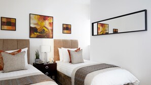 A hotel room with two beds, a nightstand with a lamp, and three abstract paintings on the wall. - Watford WD18 - Beautiful 1Bedroom/1Bathroom Flat with Free Parking & Free WIFI (Watford)