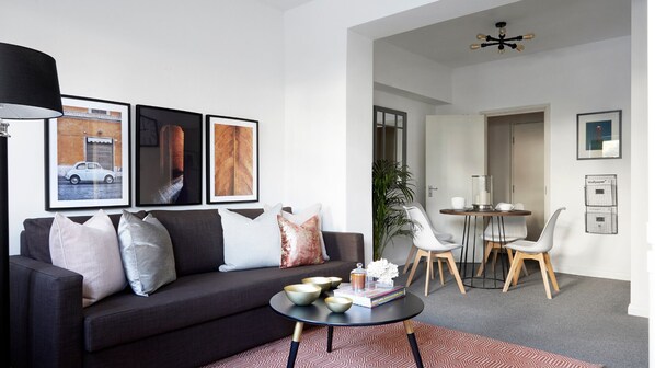 Un salon moderne avec un canapé foncé, une table basse et des œuvres d’art encadrées accroch ées au mur.