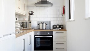 A compact kitchen with white cabinets, a stainless steel range hood, a built-in oven, and a microwave. - Watford WD18 - Beautiful 1Bedroom/1Bathroom Flat with Free Parking & Free WIFI (Watford)