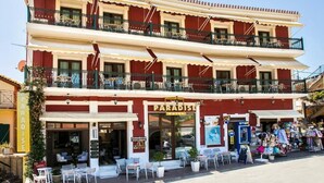 A two-story hotel with balconies, outdoor seating, and a visible storefront. - Paradise Hotel (Parga)