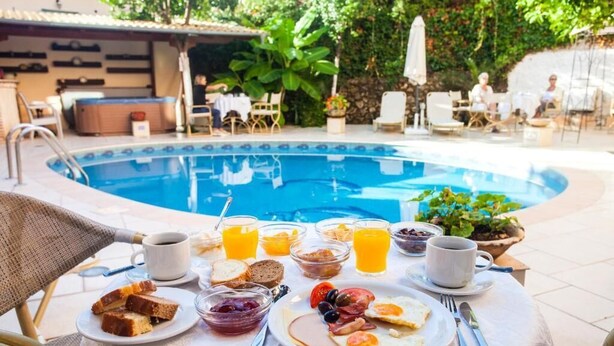 A breakfast table with a pool view, including plates of food, drinks, and a hot tub in the background. - Paradise Hotel (Parga)