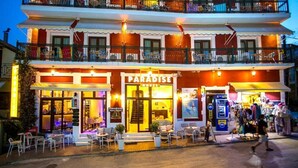 A hotel named "Paradise Hotel" with a two-story structure, outdoor seating area, and a visible ATM machine. - Paradise Hotel (Parga)