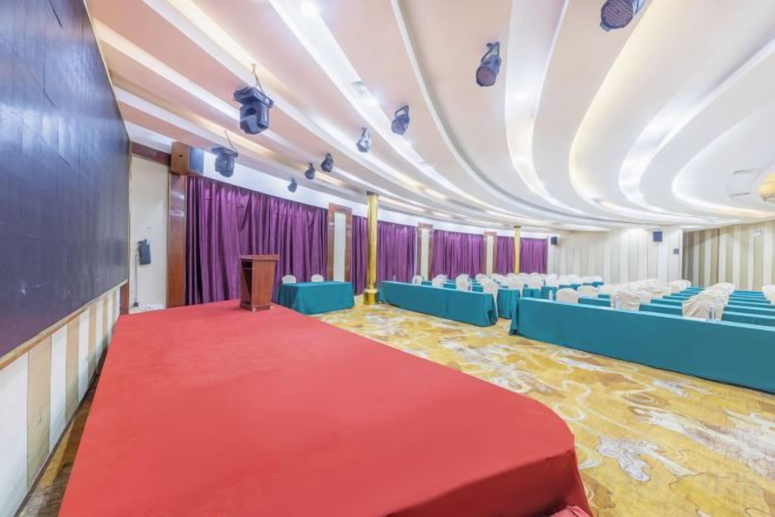 A conference room with a red carpet, a podium, and rows of blue seating.