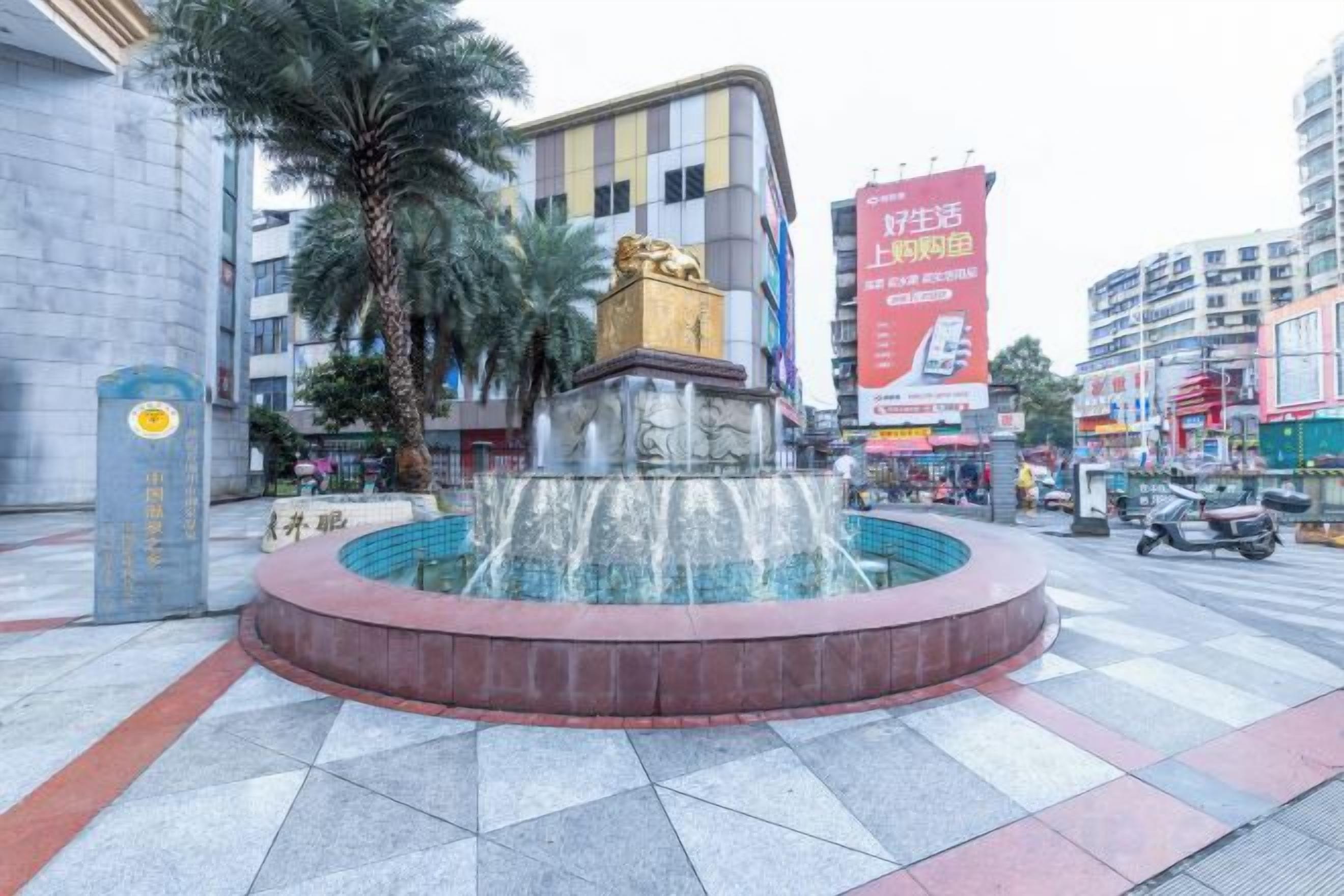 Ein öffentlicher Platz mit einem zentralen Brunnen, umgeben von Gebäuden und Palmen.