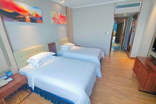 A hotel room with two beds, a wooden floor, a TV, and artwork on the wall.