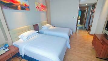 A hotel room with two beds, a wooden floor, a TV, and artwork on the wall.