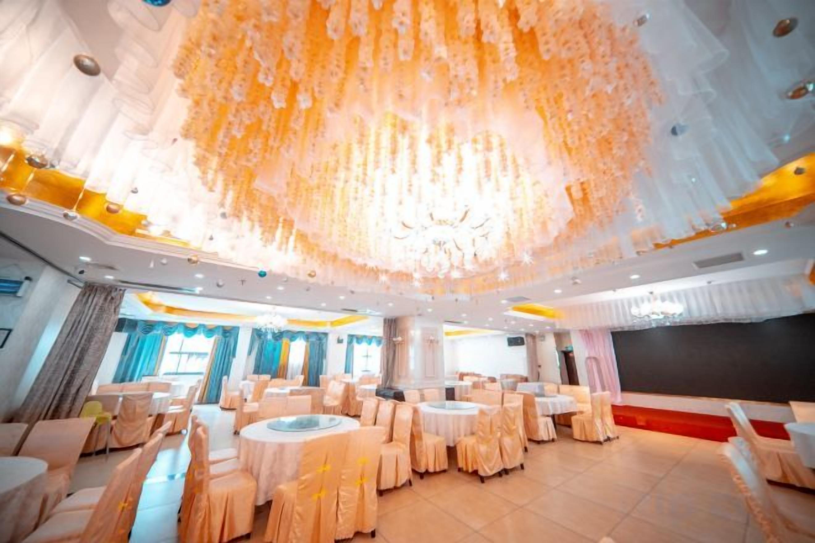 A banquet hall with round tables and chairs, a large chandelier, and a stage area.