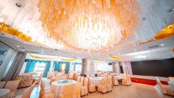 A banquet hall with round tables and chairs, a large chandelier, and a stage area.