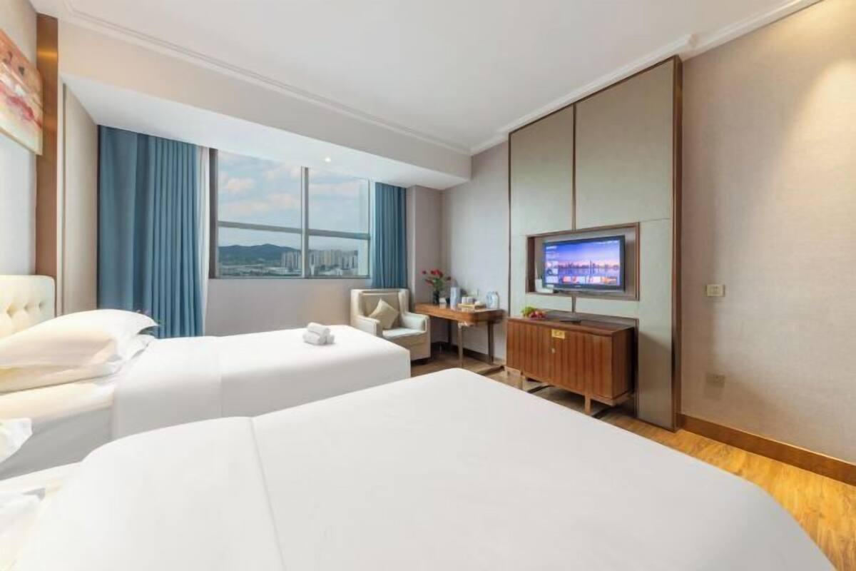 Ett hotellrum med två sängar, en tv, ett skrivbord och utsikt över stadsbilden.