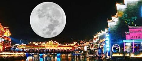 Un bâtiment traditionnel qui se reflète dans l’eau, une pleine lune dans le ciel et une enseigne avec des caractères chinois.
