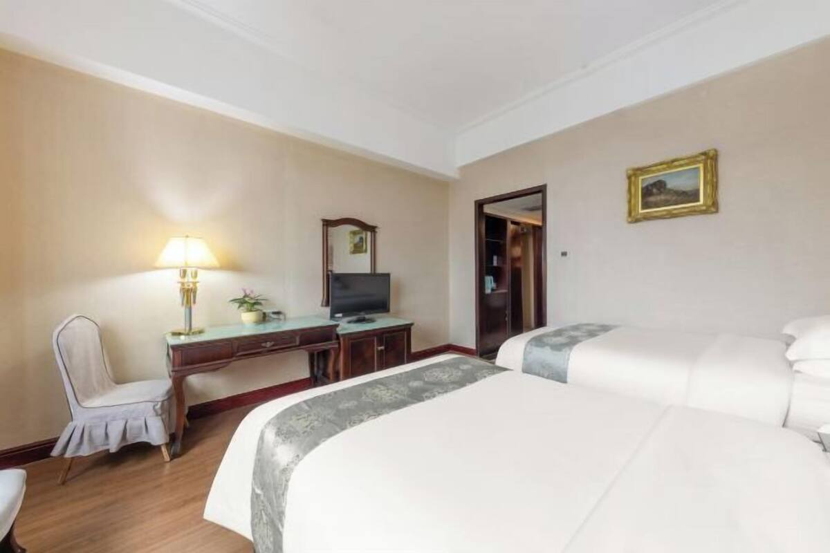 Ett hotellrum med två sängar, ett skrivbord med en lampa, en tv och en inramad tavla på väggen.