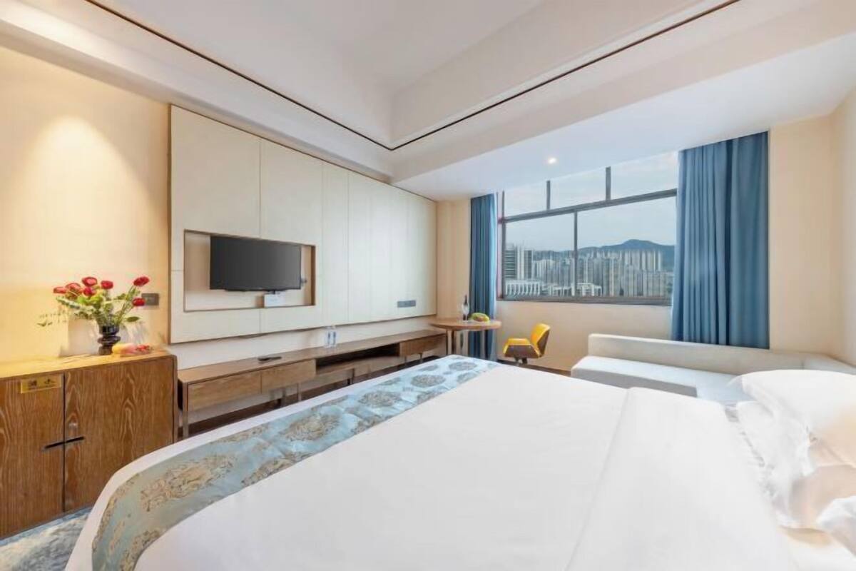 Ett modernt hotellrum med en stor säng, en platt-TV, ett skrivbord och ett fönster med utsikt över staden.