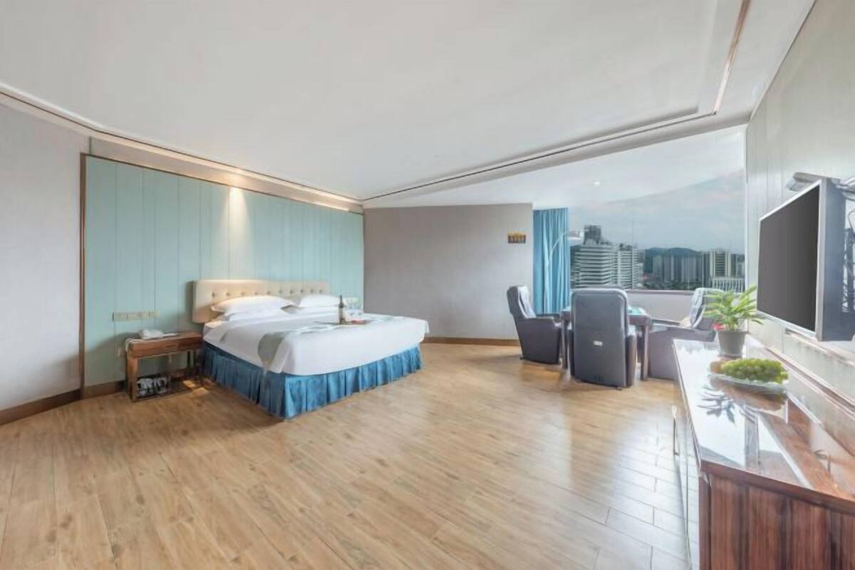 Ett hotellrum med en säng, ett skrivbord, en stol, en tv och utsikt över staden.