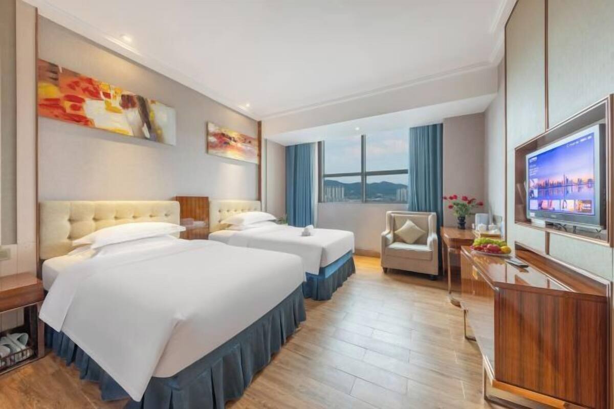 Ett hotellrum med två sängar, en TV, ett skrivbord och ett fönster med utsikt över staden.