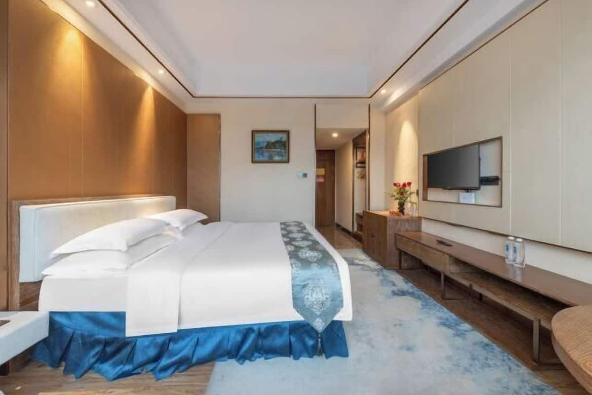 Ett modernt hotellrum med en stor säng, en platt-TV, ett skrivbord och ett badrum som syns genom en öppen dörr.