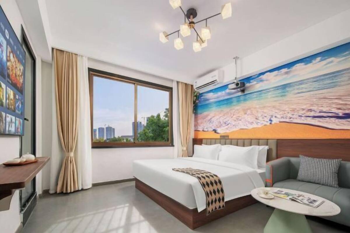 Habitación de hotel con una cama grande, un sofá, una mesita y un mural con un paisaje de playa.