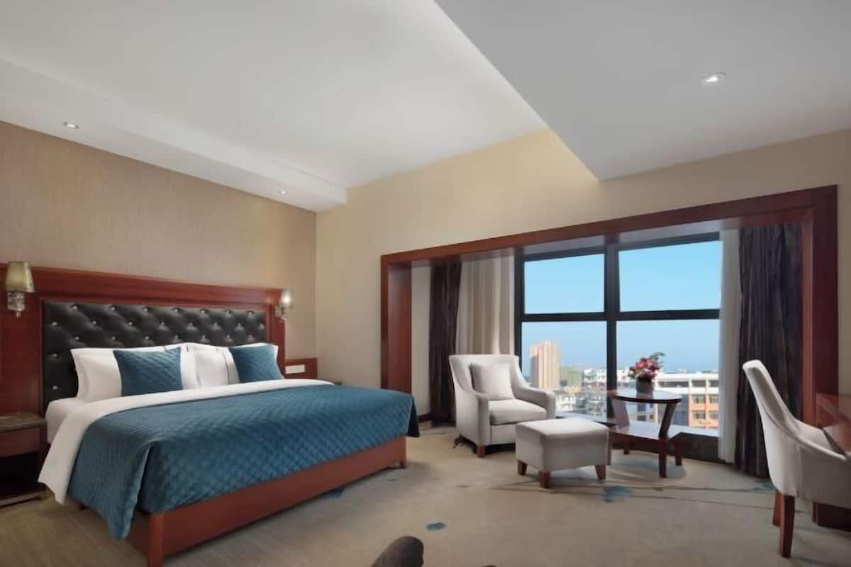 A hotel room with a large bed, a sitting area with a table and chairs, and a large window offering a view of the city.