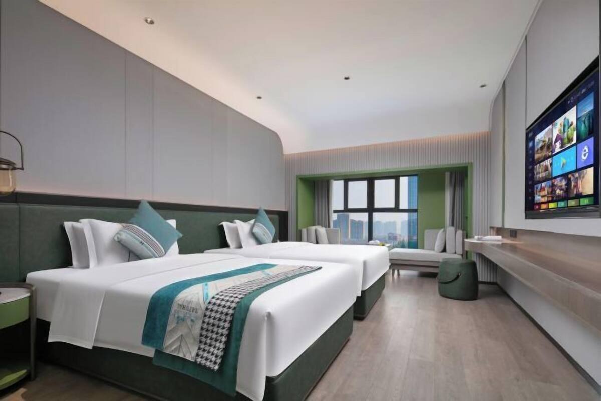Una habitación de hotel moderna con dos camas, un ventanal grande, un televisor de pantalla plana y una pared decorada en tonos verdes.