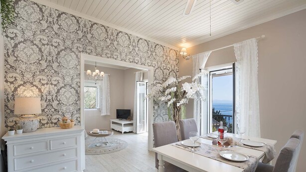 Un coin repas avec une table dressée pour deux personnes, une commode blanche, un téléviseur et une vue sur la mer par la fenêtre.