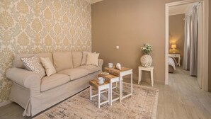 Un salon avec un canapé beige, une table basse, un papier peint à motifs et une petite table d’appoint sur laquelle est posé un vase.