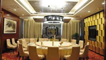 A conference room with a round table, chairs, a chandelier, and a television on the wall.