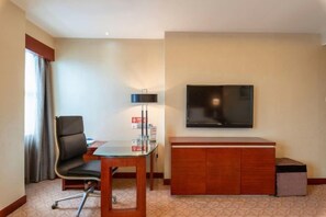A hotel room with a flat-screen TV mounted on the wall, a wooden cabinet, a glass table with a chair, and a window with curtains. - Huatian Hotel (Xiangtan)