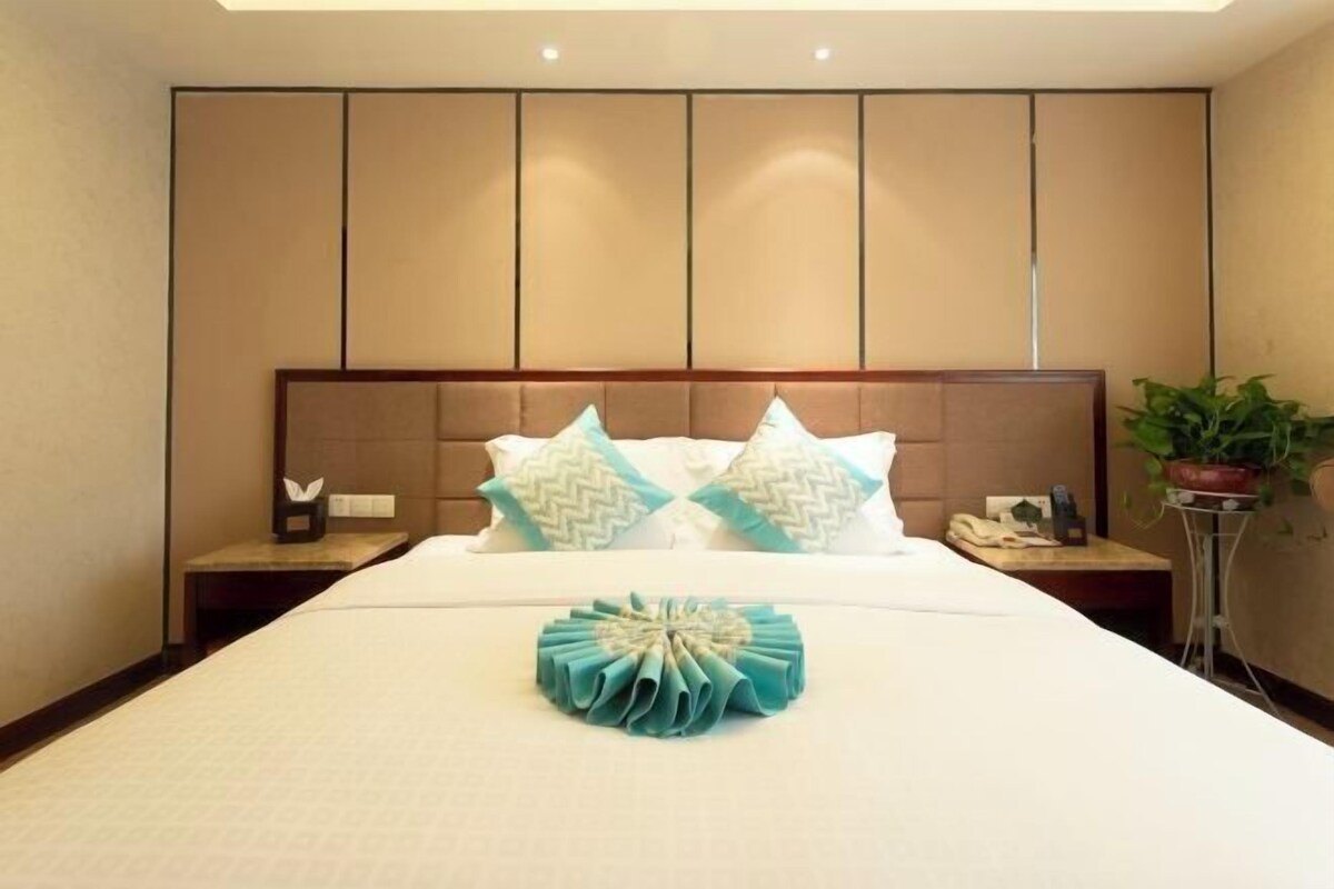 A hotel room with a large bed, a wooden headboard, and a nightstand with a lamp and a phone.
