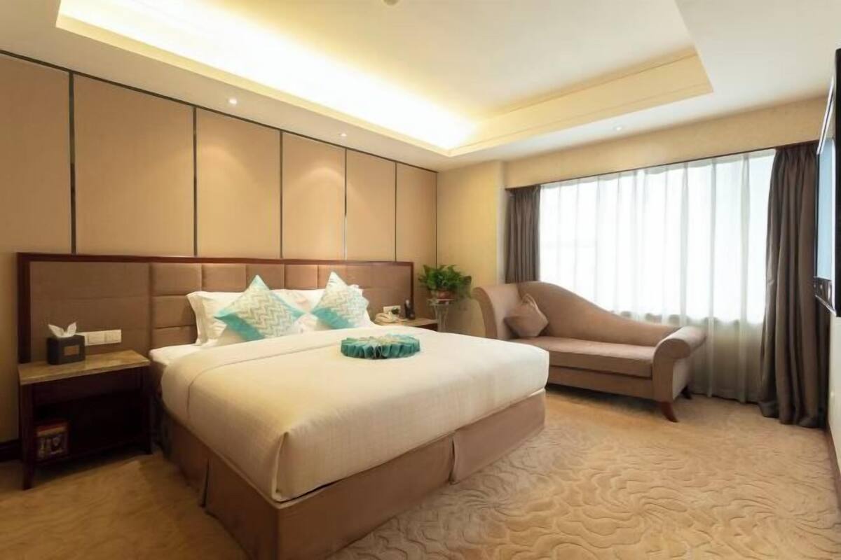 A hotel room with a large bed, a sofa, a nightstand, and a window with curtains.