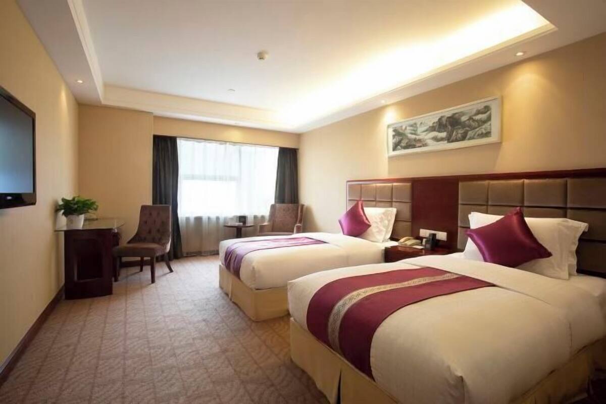 A hotel room with two beds, a desk, a chair, a television, and a window with curtains.