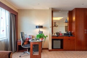 A hotel room with a desk, chair, lamp, potted plant, and a kitchenette. - Huatian Hotel (Xiangtan)