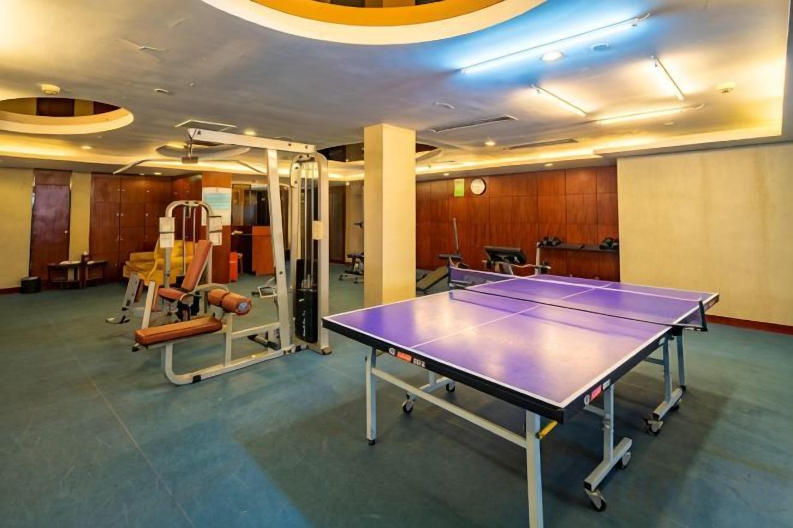 Quarto com mesa de pingue-pongue, equipamentos de ginástica e um relógio na parede.