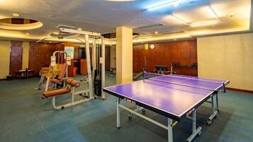 Quarto com mesa de pingue-pongue, equipamentos de ginástica e um relógio na parede.