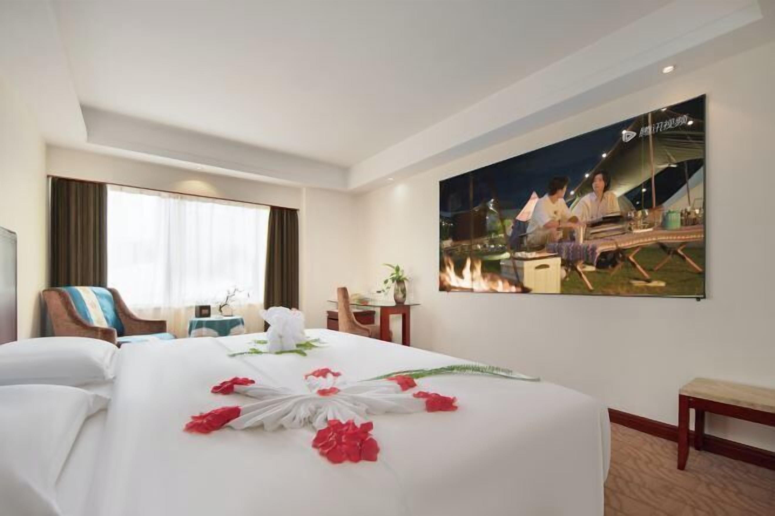 Ein Hotelzimmer mit einem großen Bett, einem Schreibtisch, einem Stuhl, einem Fenster mit Vorhängen und einem an der Wand hängenden Gemälde.