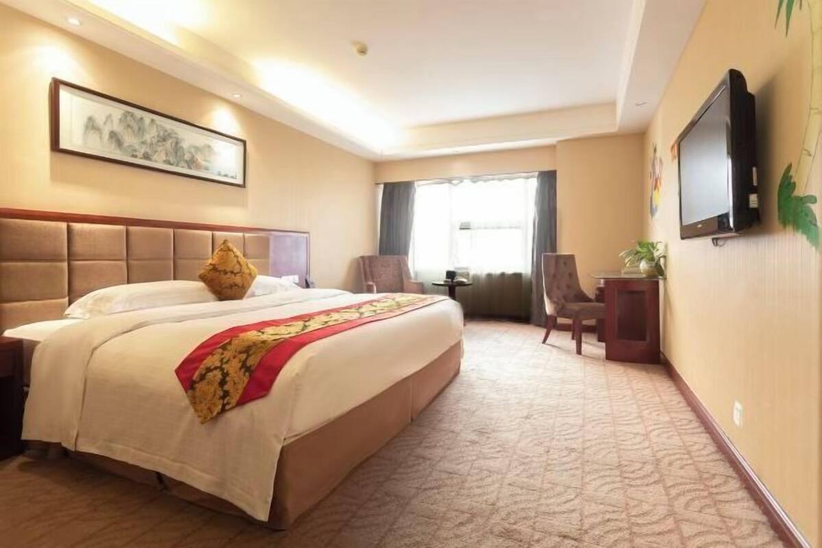 A hotel room with a large bed, a television, a desk, and a chair.