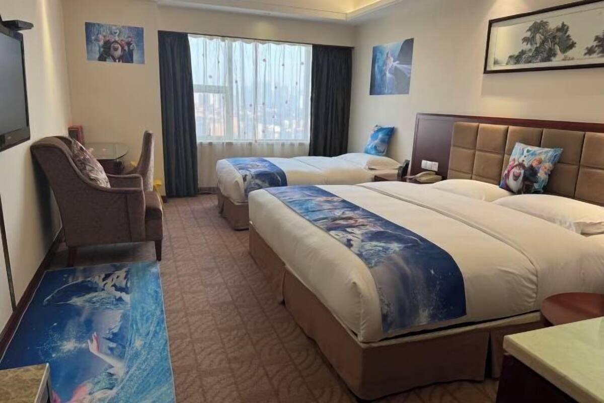 A hotel room with two beds, a desk, a chair, and a large window with curtains.