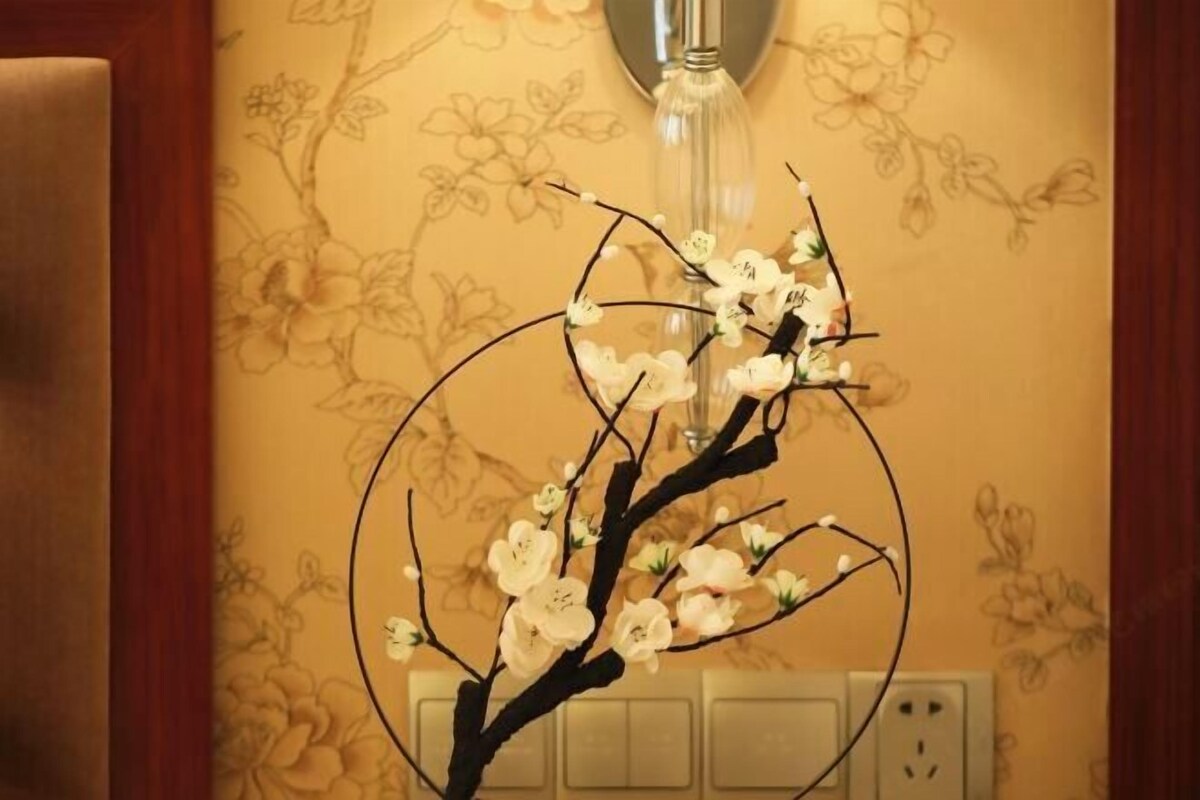 A wall with floral wallpaper and a decorative branch with white flowers.