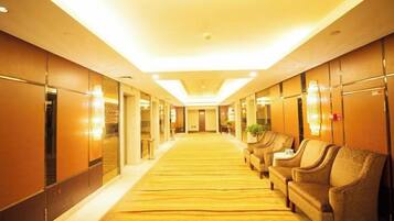 A hotel corridor with a carpeted floor, seating area with chairs, and a long hallway leading to a door.