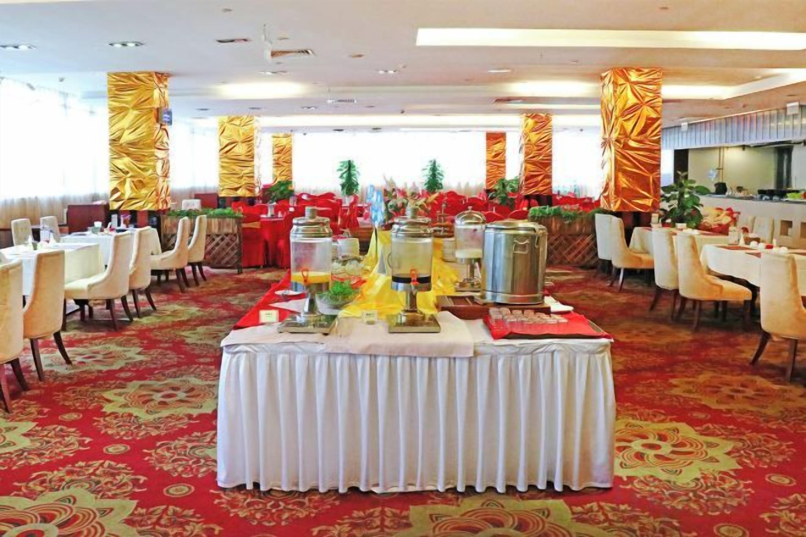 Een feestzaal met ronde tafels, stoelen en een buffet.